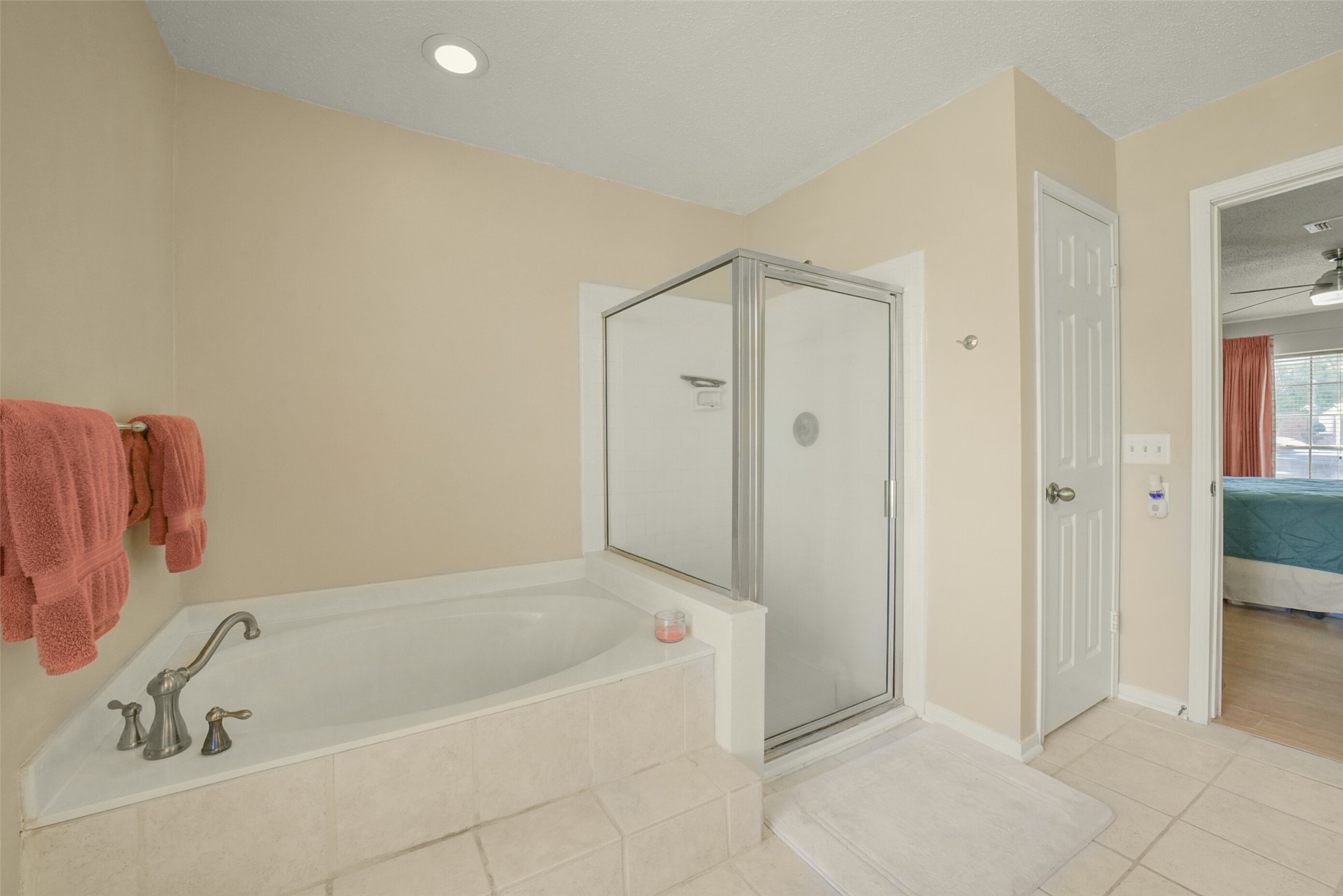 10410 Dude Road Houston, TX 77064 - Photo 21 of 45 This bathroom features a cozy corner bathtub, a glass-enclosed shower, and neutral tile flooring. It connects to a bedroom, offering convenience and comfort.