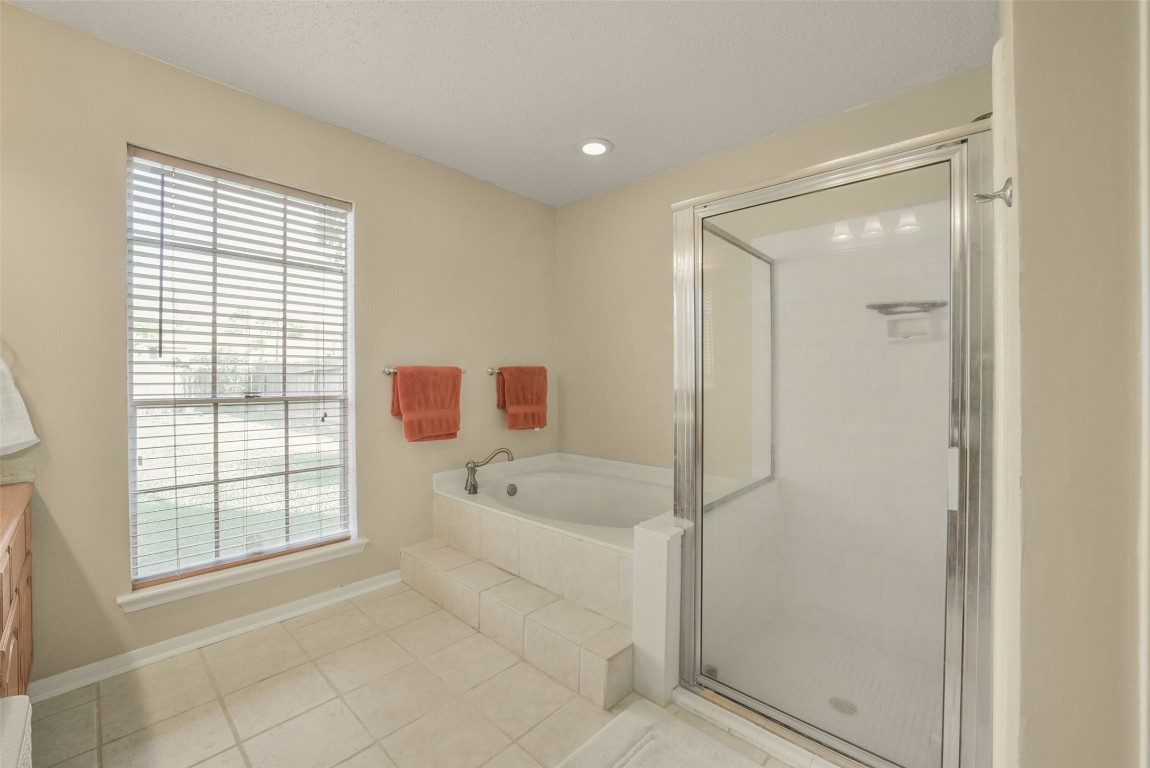 10410 Dude Road Houston, TX 77064 - Photo 22 of 45 This bathroom features a spacious walk-in shower, a corner soaking tub, and a large window for natural light. It has neutral tile flooring and walls with red towel accents, creating a clean and inviting atmosphere.