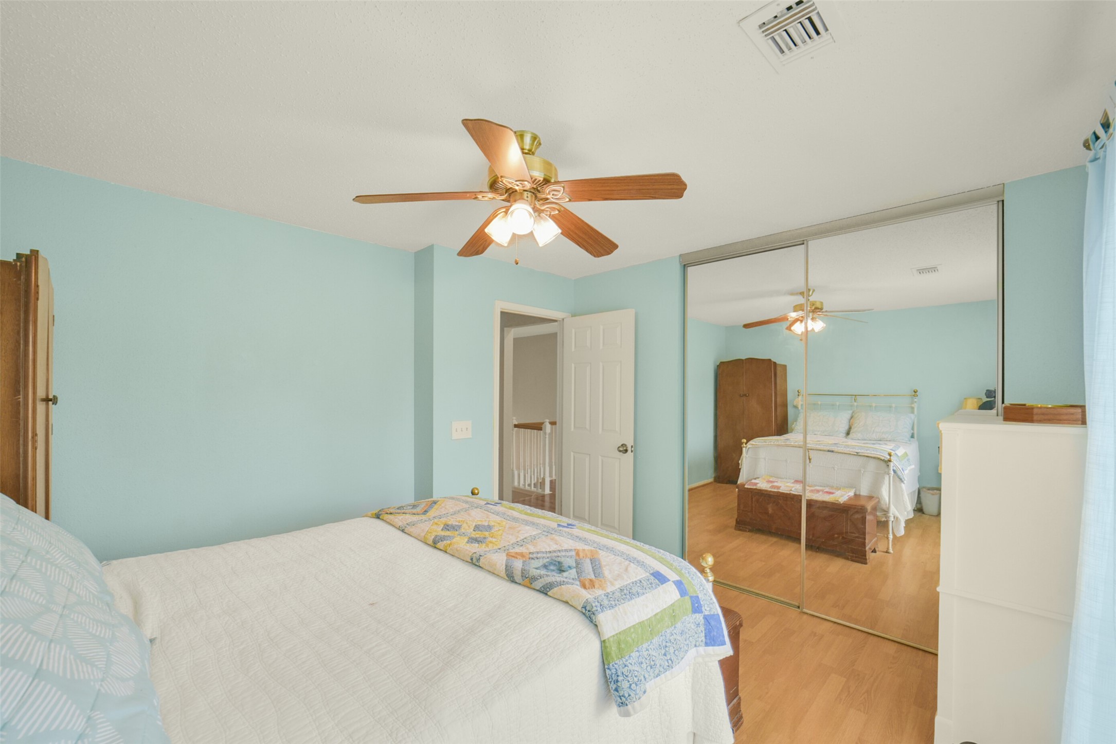 10410 Dude Road Houston, TX 77064 - Photo 30 of 45 Bright bedroom with light blue walls, a ceiling fan, and mirrored closet doors. It features a cozy bed with a colorful quilt and wooden furniture, creating a warm and inviting atmosphere.