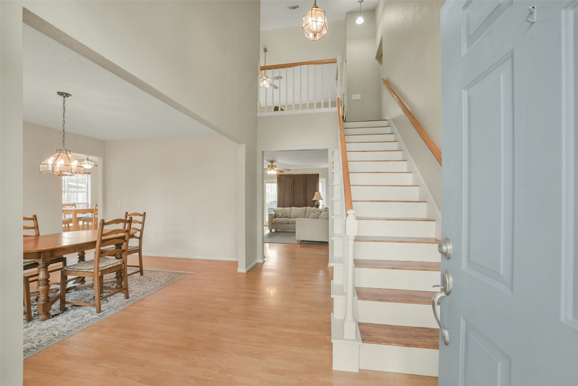 10410 Dude Road Houston, TX 77064 - Photo 3 of 45 This inviting entryway features a warm wood floor leading to a carpeted staircase with white railings. To the left is a bright dining area with a wooden table under elegant pendant lighting. The open layout flows into a cozy living room, perfect for family gatherings.