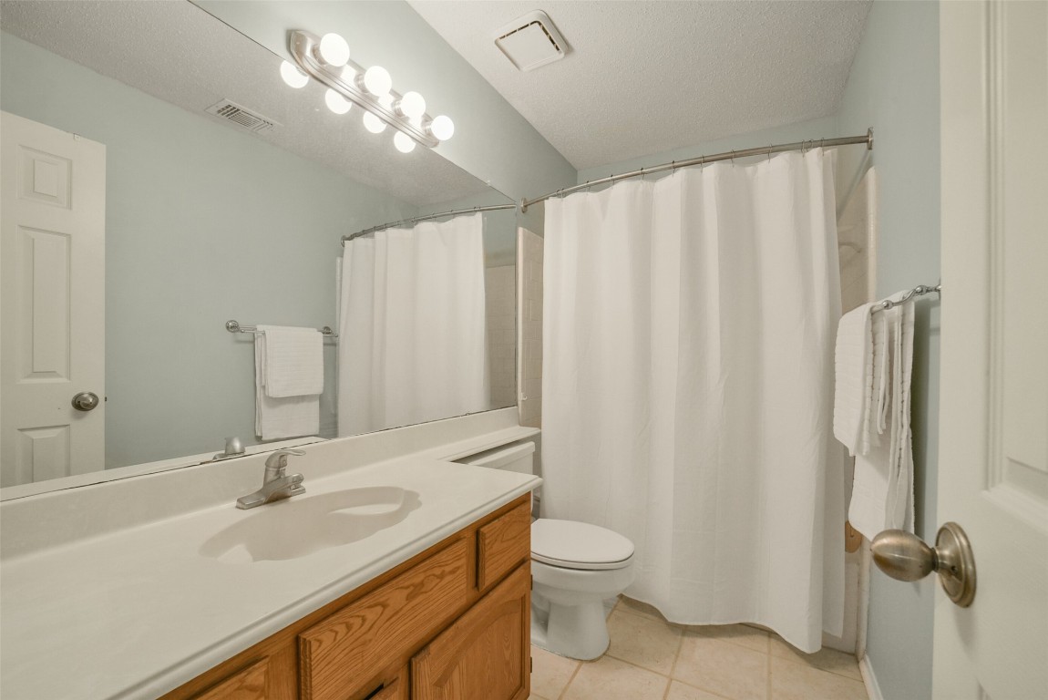 10410 Dude Road Houston, TX 77064 - Photo 31 of 45 This bathroom features a light color scheme with a large mirror above a wooden vanity. It includes a standard bathtub with a white shower curtain and tile flooring, creating a clean and bright atmosphere.