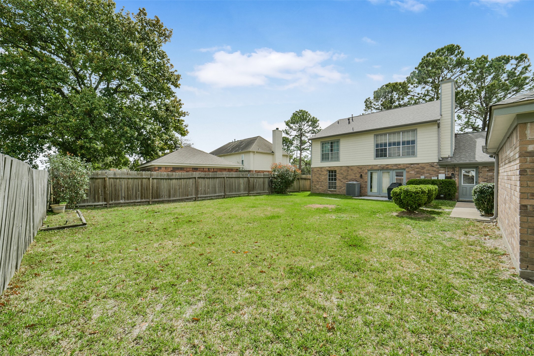 10410 Dude Road Houston, TX 77064 - Photo 34 of 45 Spacious backyard with a well-maintained lawn, bordered by a wooden fence for privacy. The two-story house features brick and siding exterior, large windows, and a patio area, offering a perfect setting for outdoor activities and relaxation.