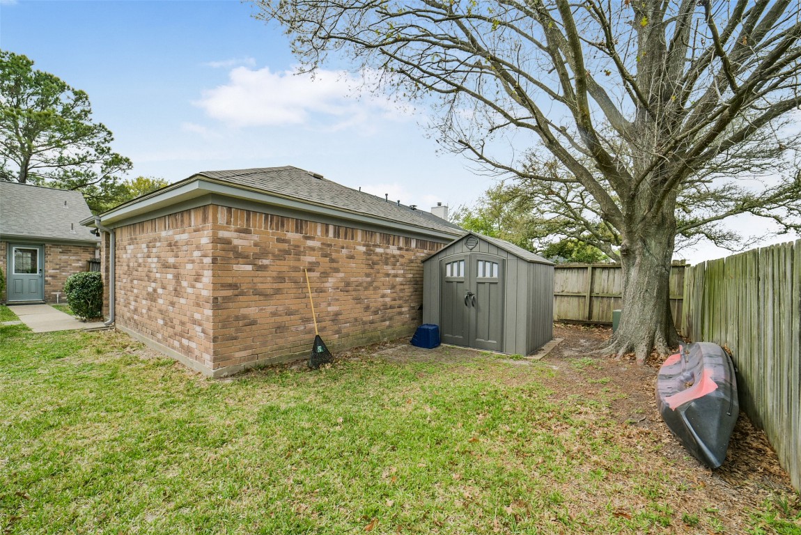 10410 Dude Road Houston, TX 77064 - Photo 35 of 45 This backyard features a brick exterior, a spacious grassy area, a sturdy wooden fence, and a large tree providing shade. A storage shed offers additional space for tools or outdoor equipment.