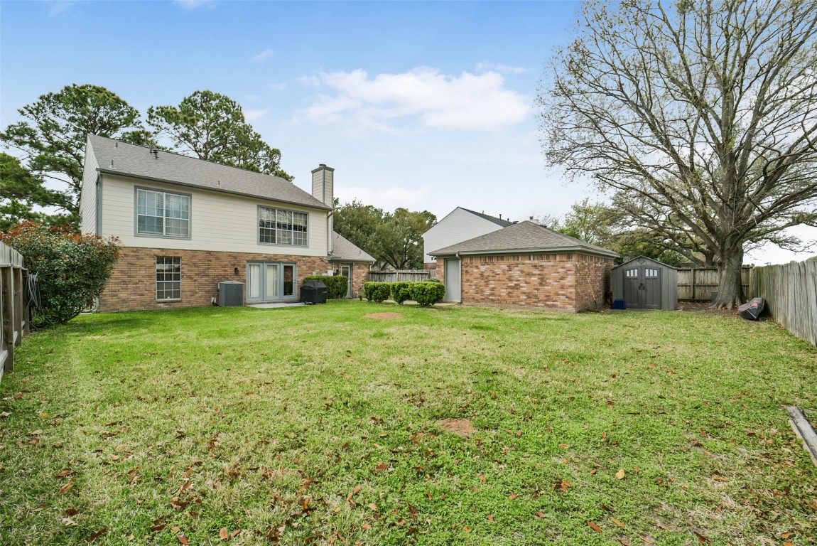 10410 Dude Road Houston, TX 77064 - Photo 36 of 45 This photo showcases a spacious backyard with a well-maintained lawn, surrounded by a wooden fence. The house features a brick exterior with large windows and a patio area. There's also a detached brick garage and a storage shed, ideal for outdoor needs. Mature trees provide shade and a serene atmosphere.
