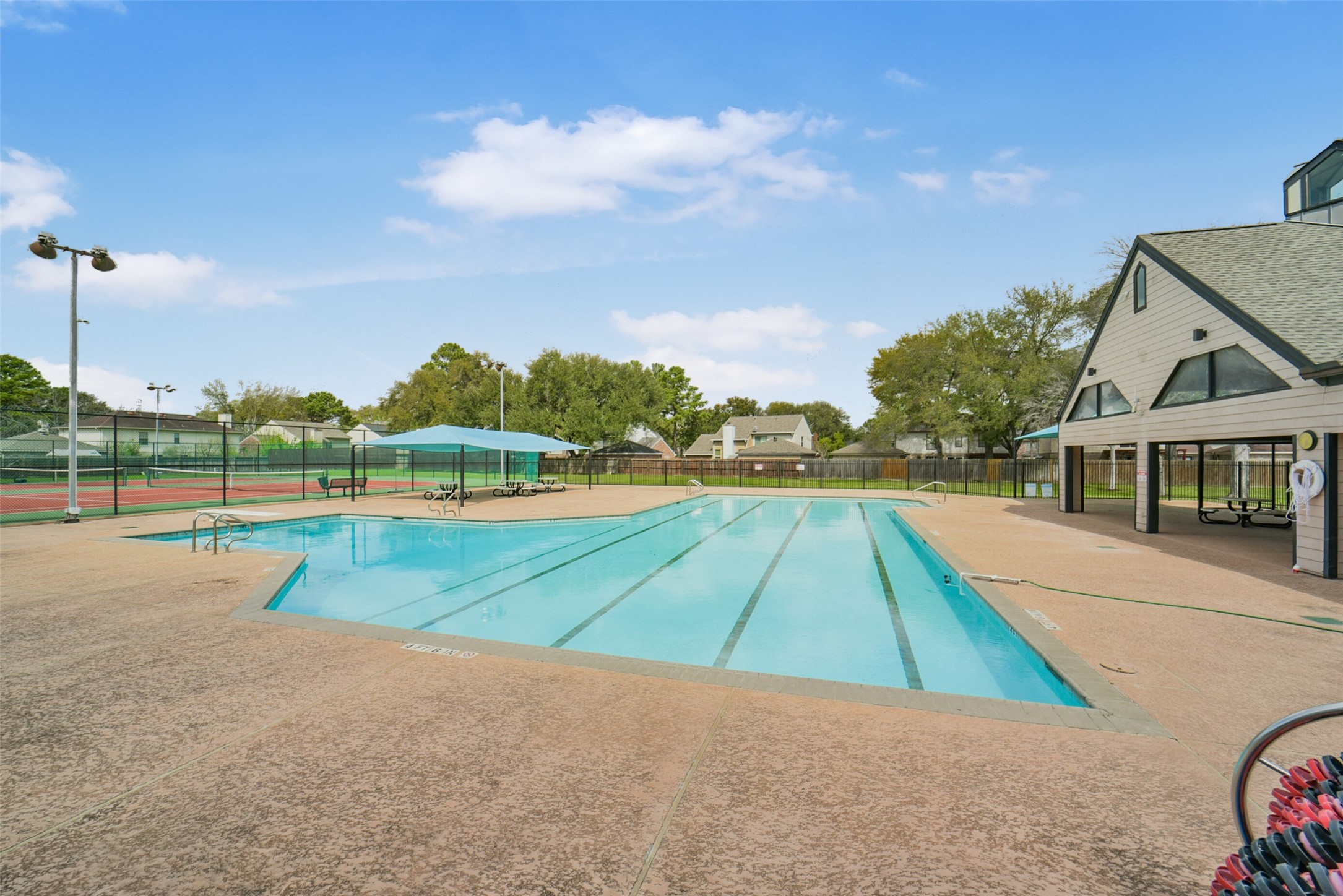 10410 Dude Road Houston, TX 77064 - Photo 42 of 45 This photo showcases a community recreational area featuring a large outdoor swimming pool with lap lanes, adjacent to a covered pavilion. The space is surrounded by a tennis court and greenery, offering a welcoming environment for relaxation and outdoor activities.
