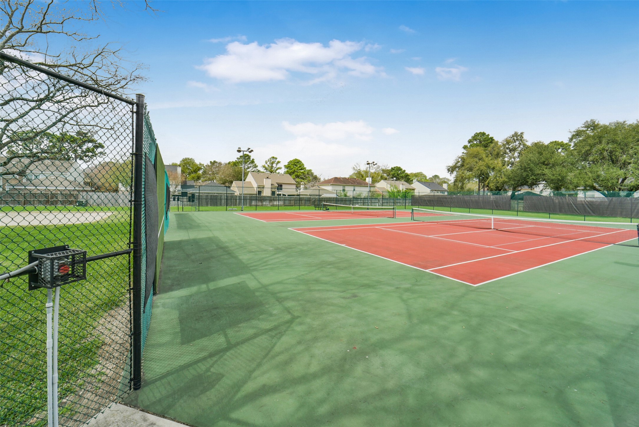 10410 Dude Road Houston, TX 77064 - Photo 43 of 45 This photo shows a well-maintained tennis court within a residential community, surrounded by a chain-link fence and lush greenery. Ideal for active living.