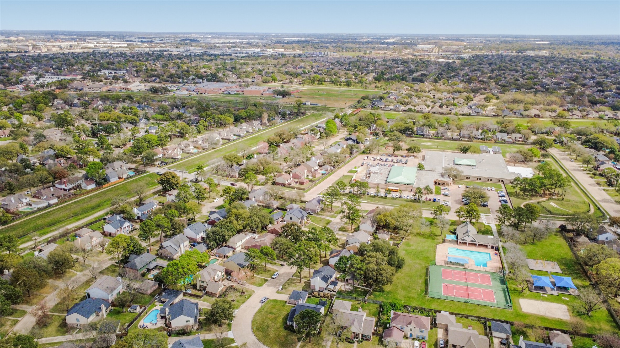 10410 Dude Road Houston, TX 77064 - Photo 45 of 45 This aerial photo showcases a suburban neighborhood with tree-lined streets and neatly arranged homes. It features nearby amenities like tennis courts and a pool, with a large community building and expansive greenery, offering a peaceful residential atmosphere.