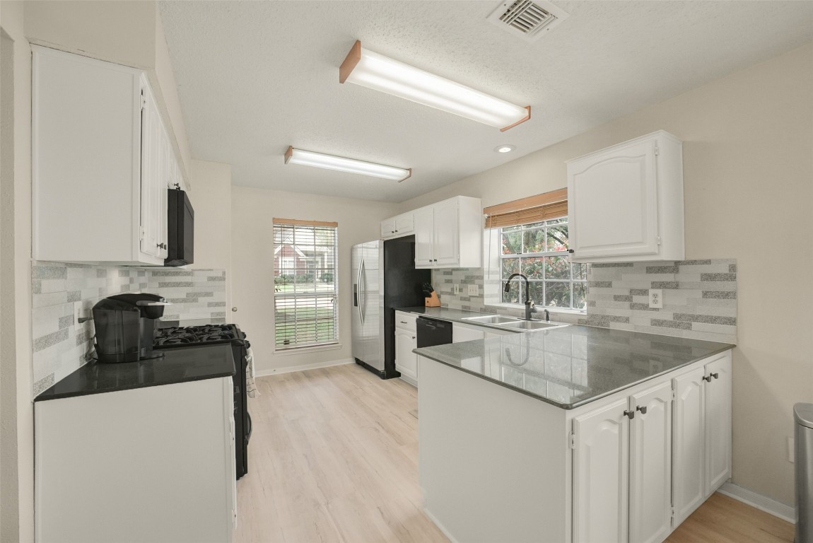 10410 Dude Road Houston, TX 77064 - Photo 7 of 45 Bright, modern kitchen with white cabinetry, light wood flooring, and ample natural light from large windows. Features include stainless steel appliances, a stylish tile backsplash, and a spacious countertop area for cooking and entertaining.
