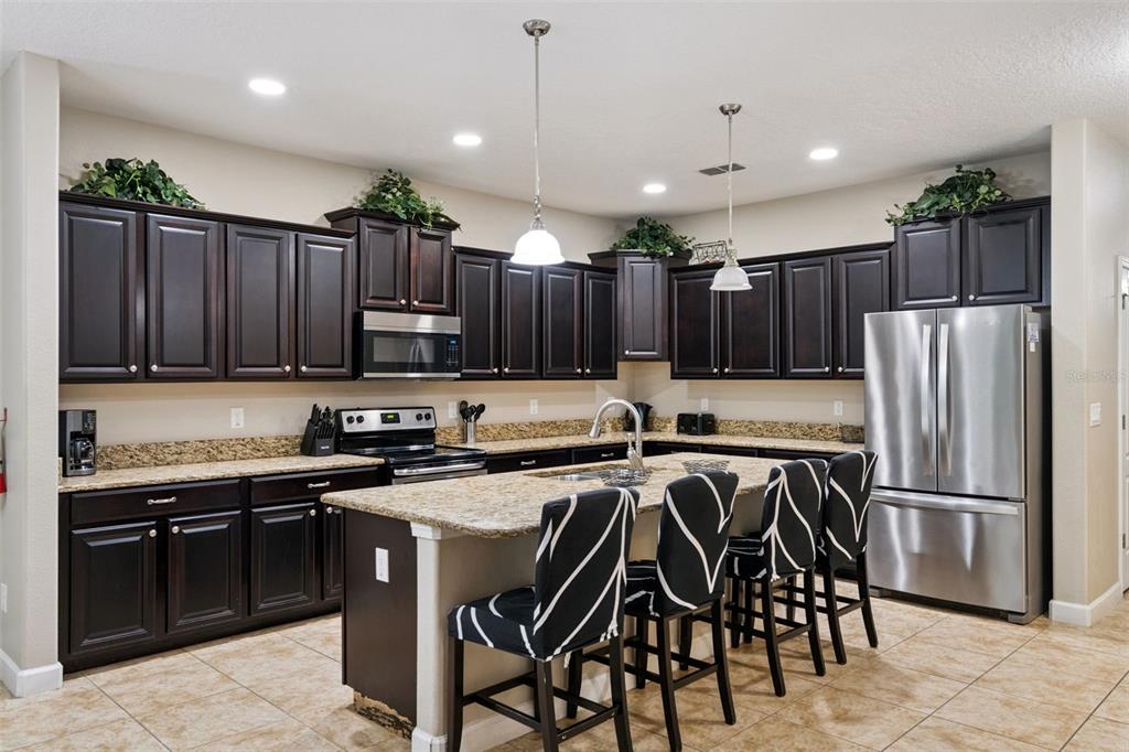 8965 Cuban Palm Road Kissimmee, FL 34747 - Photo 11 of 77 a kitchen with kitchen island granite countertop stainless steel appliances a sink a stove a refrigerator cabinets and chairs
