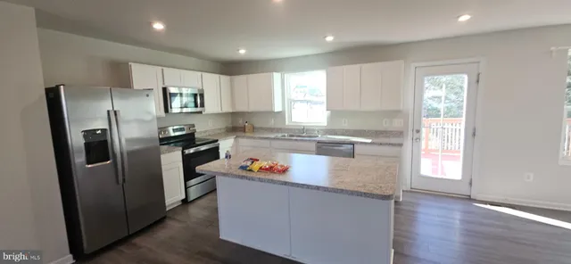 a kitchen with stainless steel appliances granite countertop a refrigerator a sink a stove and white cabinets with wooden floor