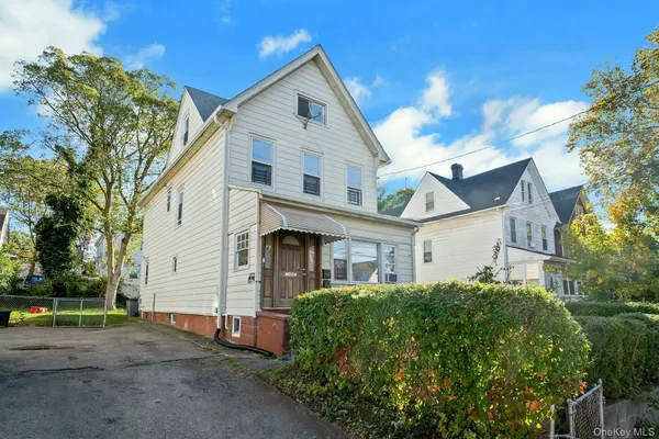a view of a white house next to a yard with big trees