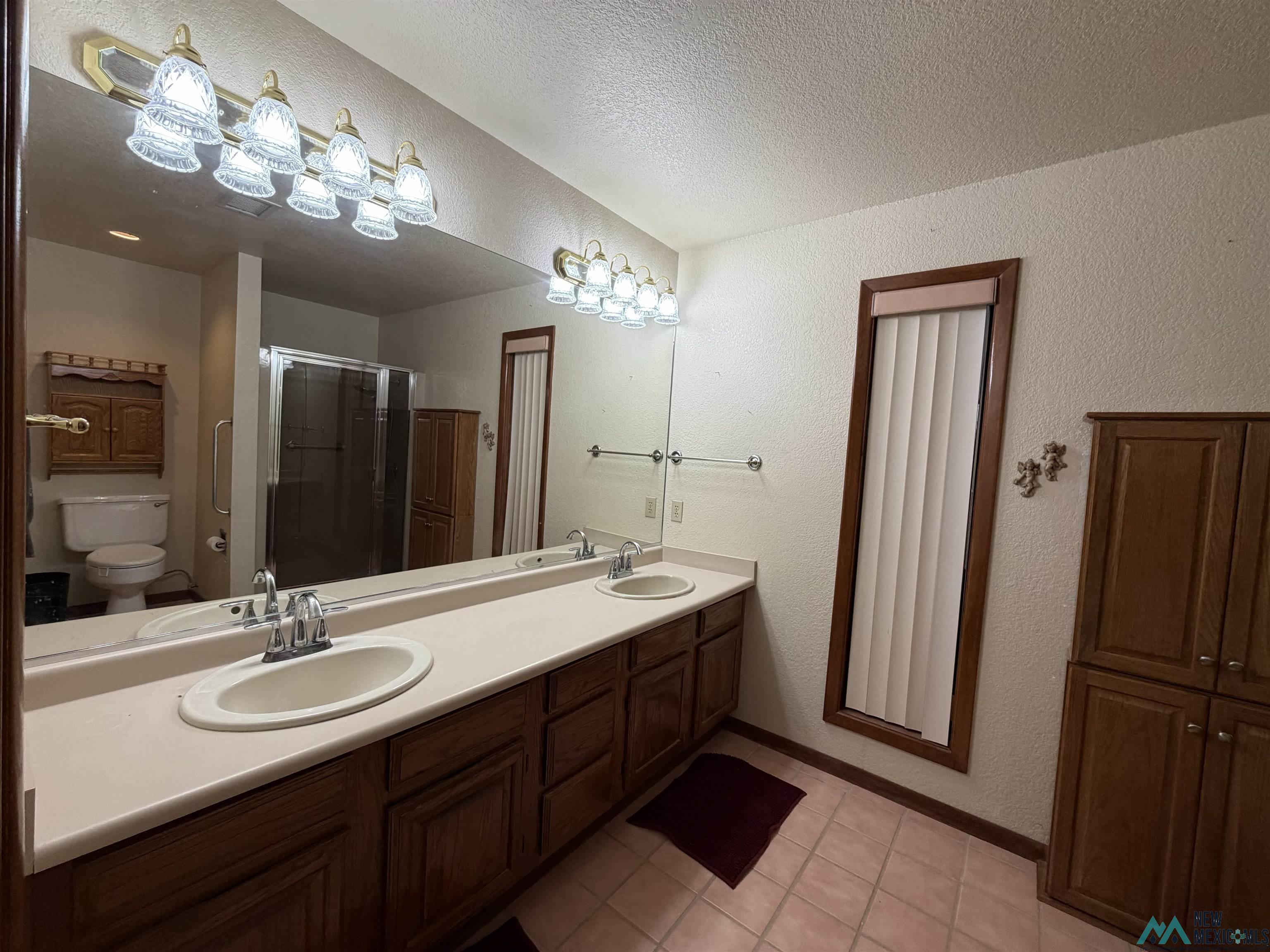 2001 East Derrick Road Carlsbad, NM 88220 - Photo 75 of 84 Bathroom featuring a textured wall, a stall shower, double vanity, a textured ceiling, and light tile patterned floors