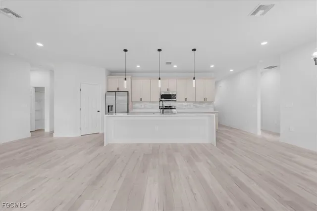 a large white kitchen with kitchen island a sink dishwasher a refrigerator and white cabinets with wooden floor