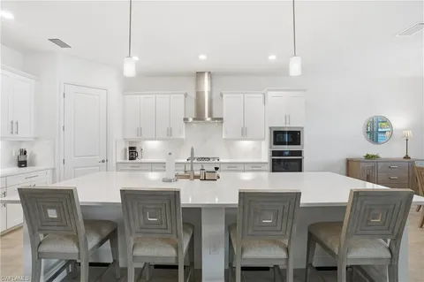 a kitchen with stainless steel appliances kitchen island granite countertop a dining table chairs and white cabinets