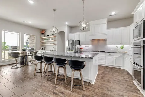 a kitchen with stainless steel appliances kitchen island granite countertop a stove a sink a dining table and chairs with wooden floor