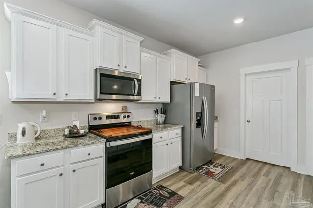 a kitchen with granite countertop a refrigerator stove and white cabinets