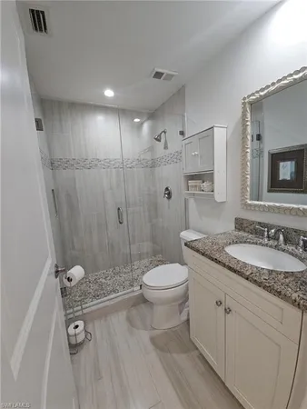 a bathroom with a granite countertop sink a toilet a mirror and shower