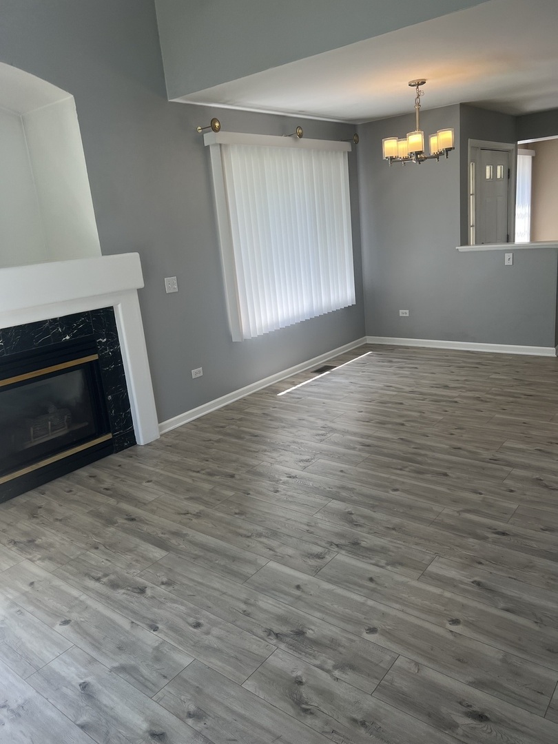 945 Huntington Drive, Unit 945 Elk Grove Village, IL 60007 - Photo 5 of 9 an empty room with wooden floor fireplace and windows
