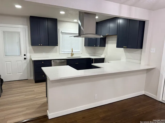 a large kitchen with stainless steel appliances a large counter top a stove and a wooden floor