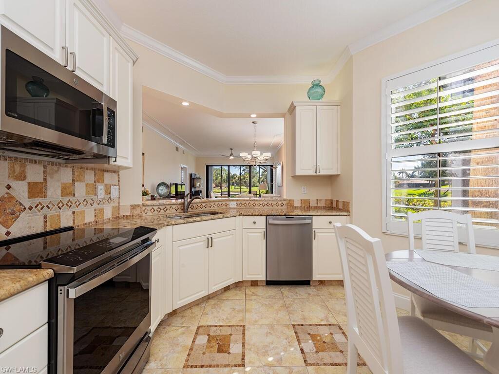 2433 Ravenna Boulevard, Unit 102 Naples, FL 34109 - Photo 5 of 12 Kitchen with backsplash, a sink, stainless steel appliances, crown molding, and a notable chandelier