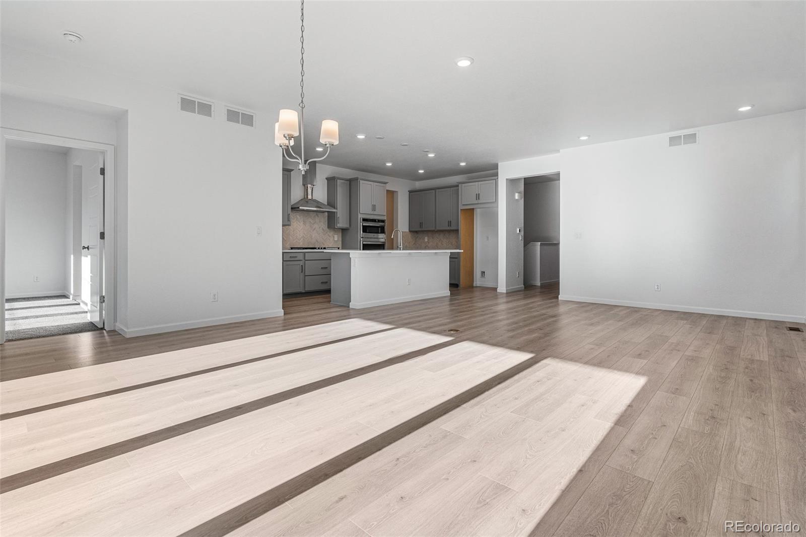 23936 River Front Drive Aurora, CO 80019 - Photo 5 of 46 a large kitchen with kitchen island a refrigerator a stove a sink and white cabinets with wooden floor