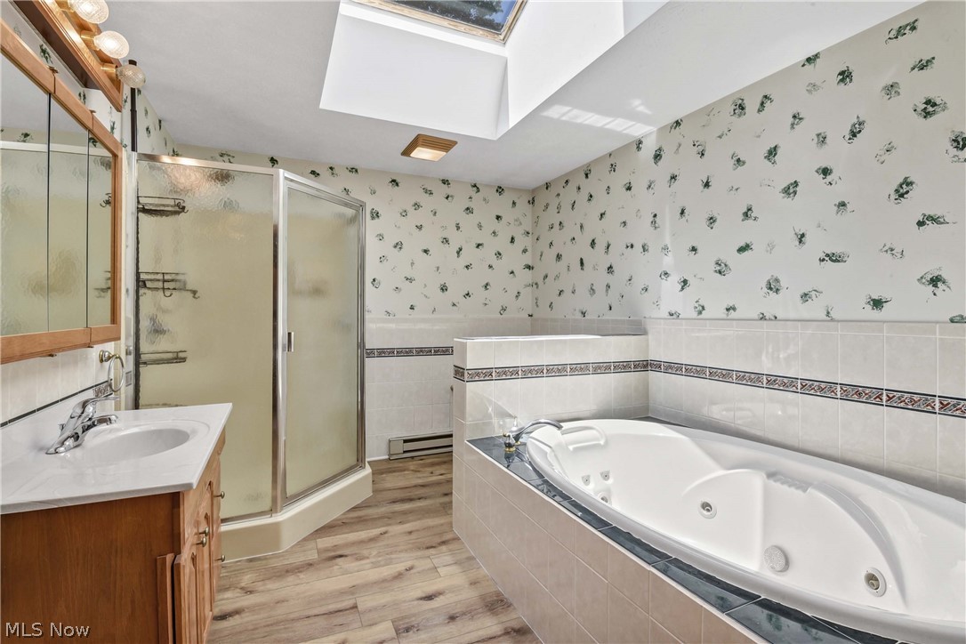 301 Crosse Road Amherst, OH 44001 - Photo 29 of 49 Bathroom featuring a built-in jetted tub, a separate glass-enclosed shower, a wood-finish vanity with an integrated sink, skylight, and wood-finish flooring