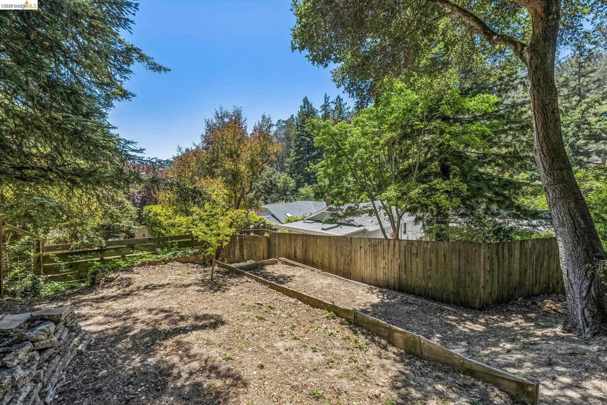 6645 Heather Ridge Way Oakland, CA 94611 - Photo 56 of 61 Tiered backyard area featuring a wood fence, mature perimeter trees, a dry-stacked stone retaining wall, and a sloped terrain