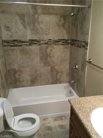 a bathroom with a granite countertop bathtub shower sink vanity and toilet