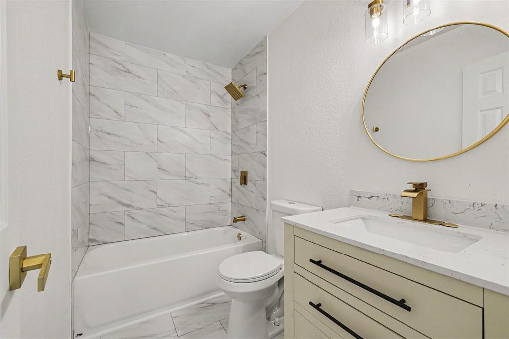 307 Dixon Street Terrell, TX 75160 - Photo 26 of 32 Bathroom featuring a white bathtub with subway tile surround, a gold-framed circular mirror, an integrated sink vanity with a light-colored countertop, and gold-finish fixtures