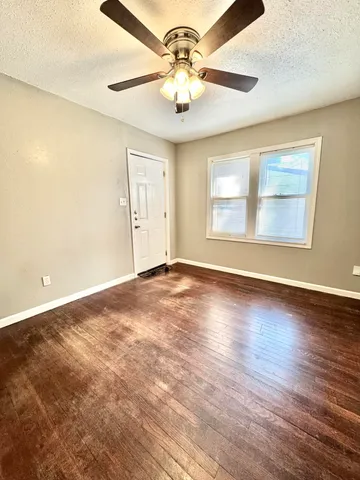 an empty room with wooden floor chandelier fan and windows
