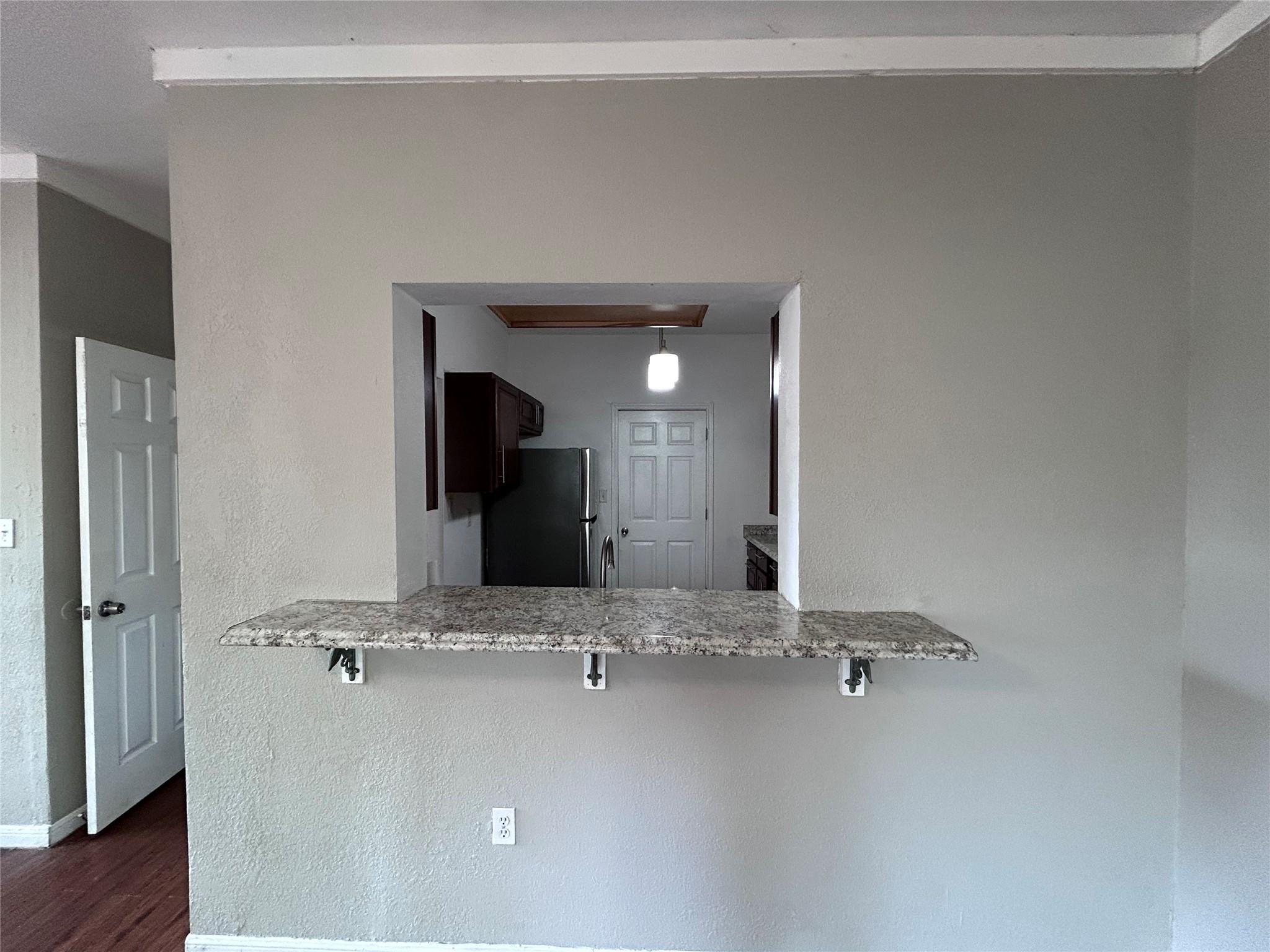 5708 Spring Meadow Road, Unit B Austin, TX 78744 - Photo 5 of 23 Kitchen with a kitchen bar, light stone counters, freestanding refrigerator, a textured wall, and a peninsula