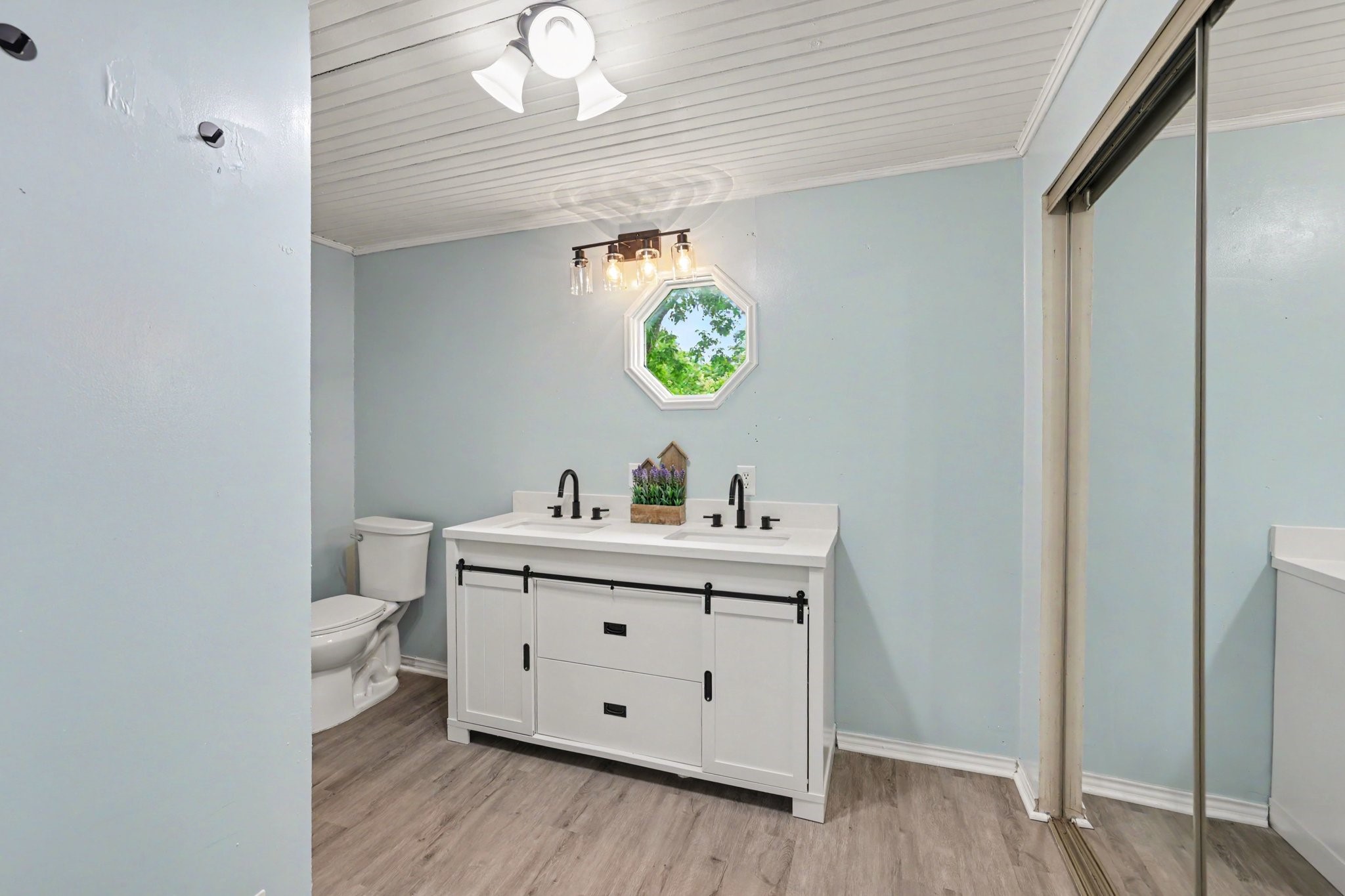 31730 Waller Tomball Road Waller, TX 77484 - Photo 28 of 50 Bright bathroom with light blue walls and luxury vinyl flooring. Features a white double vanity with black fixtures, a unique octagonal window. Primary bathroom Includes a sliding mirrored closet doors.