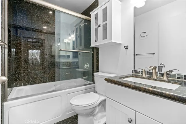 a bathroom with a granite countertop sink a toilet a mirror and shower