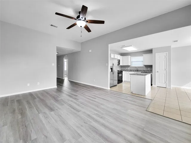 a view of an empty room and kitchen with wooden floor
