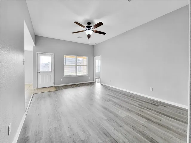an empty room with wooden floor fan and windows