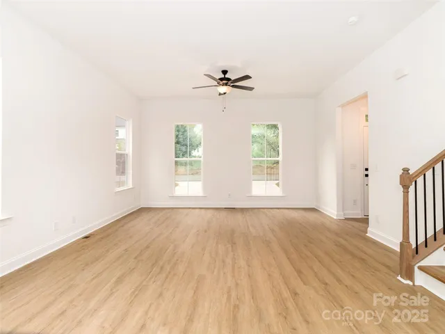 an empty room with wooden floor ceiling fan and windows