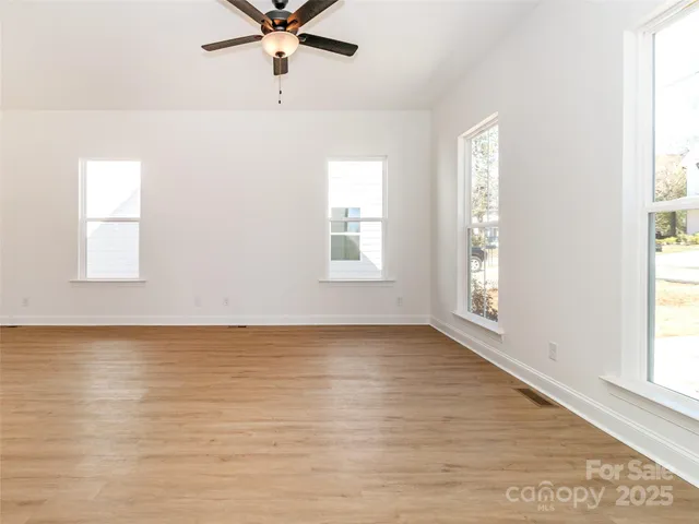 an empty room with wooden floor fan and windows