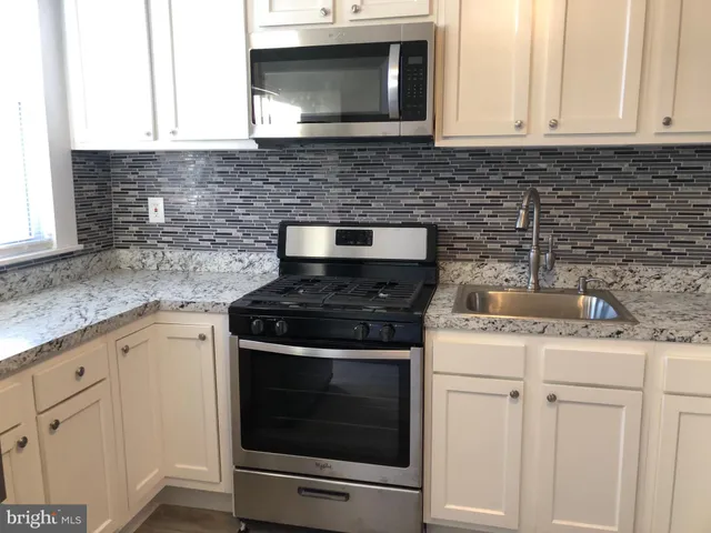 a kitchen with granite countertop white cabinets appliances and a sink