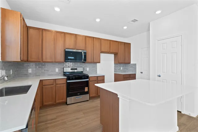 a kitchen with stainless steel appliances a stove a sink a microwave a refrigerator a sink and cabinets