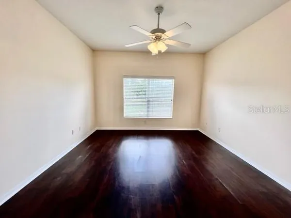 an empty room with wooden floor fan and windows
