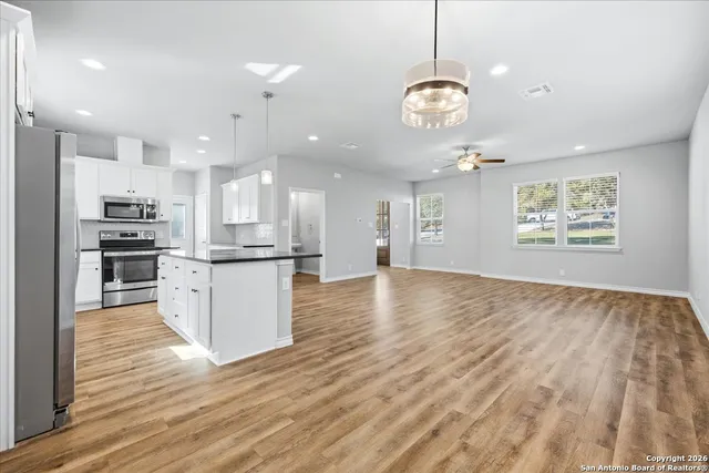 a view of a kitchen with kitchen island granite countertop wooden floor stainless steel appliances and a chandelier