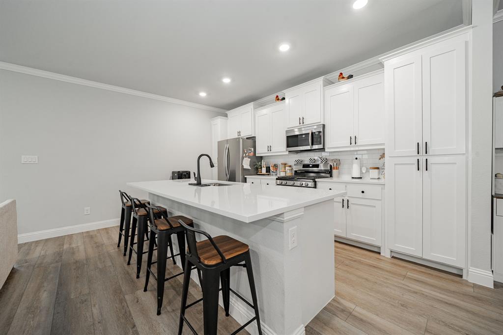 248 Waters Rdg Drive Lavon, TX 75166 - Photo 6 of 36 Kitchen with white cabinets, a breakfast bar area, a center island with sink, stainless steel appliances, and tasteful backsplash