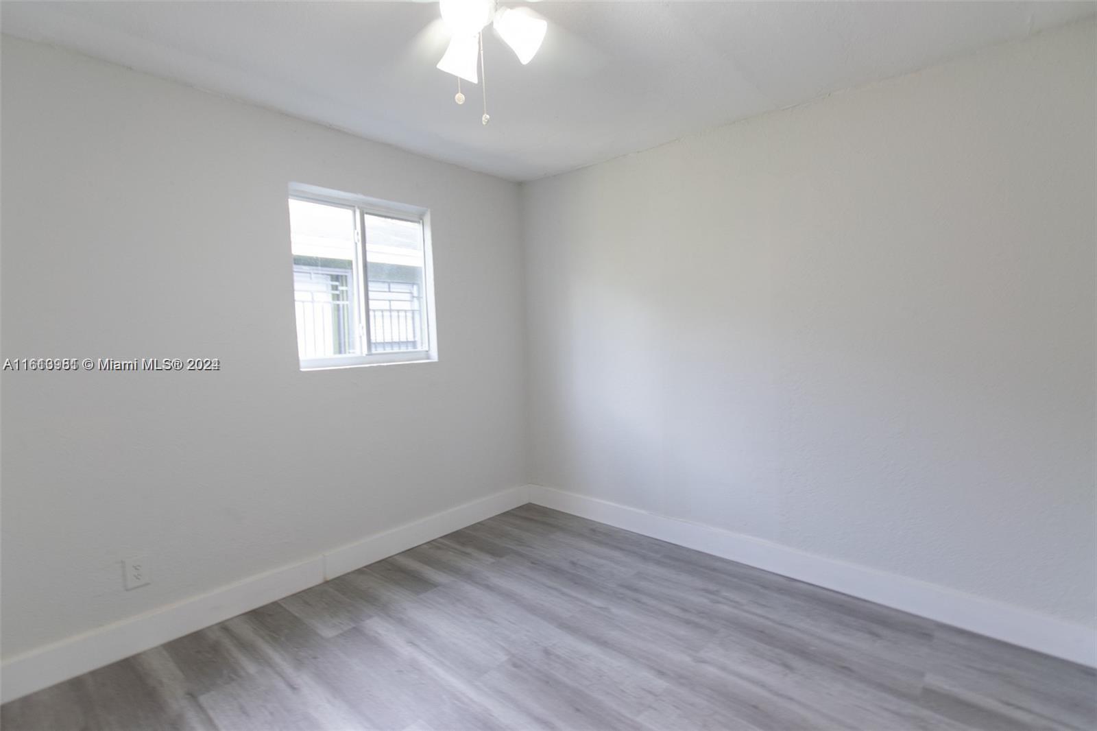 1113 Northwest 103rd Street, Unit 1 Miami, FL 33150 - Photo 9 of 12 an empty room with wooden floor and windows