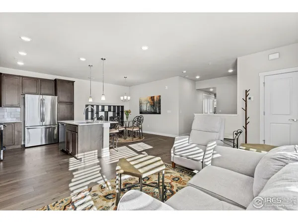 a open kitchen with stainless steel appliances granite countertop a refrigerator a stove a sink dishwasher a dining table and chairs with wooden floor