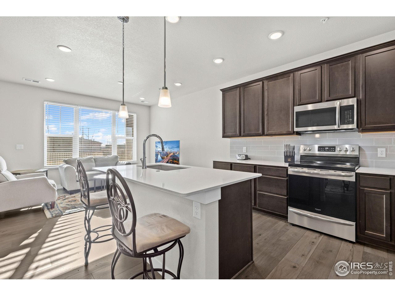 330 High Point Drive, Unit B103 Longmont, CO 80504 - Photo 10 of 18 a kitchen with stainless steel appliances kitchen island granite countertop a stove a sink a microwave a dining table and chairs