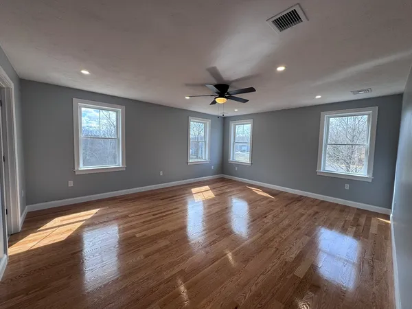 a view of empty room with wooden floor and fan