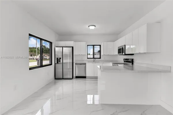 a large white kitchen with stainless steel appliances a sink a microwave a stove and white cabinets