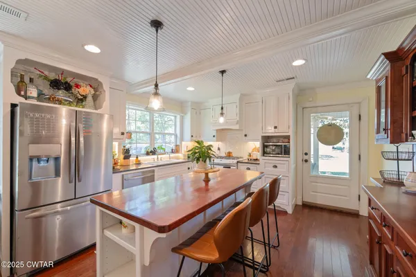 a kitchen with stainless steel appliances granite countertop a refrigerator a sink dishwasher a stove and a dining table with wooden floor