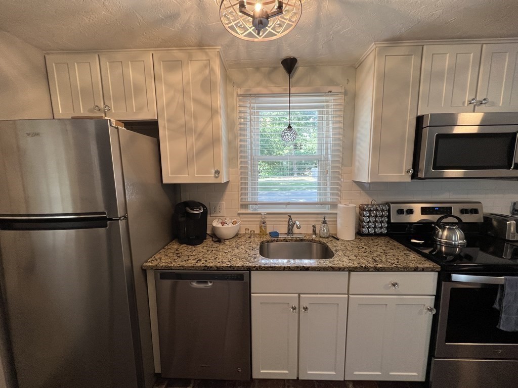 a kitchen with granite countertop a refrigerator a sink a stove a microwave and cabinets