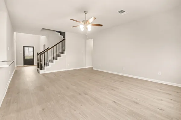 a view of an empty room with wooden floor and a ceiling fan